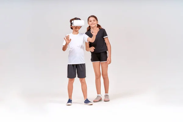 Wirtualna rzeczywistość i sport. Dwa podekscytowany nastolatek, chłopiec w okularach 3D i słodkie dziewczyny stoi odizolowany na szarym tle i zabawy — Zdjęcie stockowe