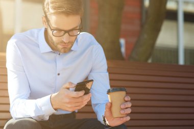 İş mesajı. Akıllı telefon kullanan ve bankta otururken kahve içen odaklanmış bir işadamı.