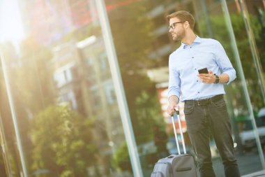 Taksi bekliyorum. Bavulunda akıllı telefon taşıyan ve havaalanının dışında duran zarif yakışıklı iş adamı.