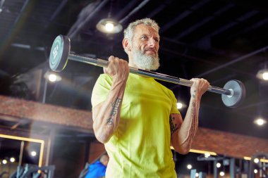 Ağırlık çalışması. Spor kıyafetli güçlü bir adam spor salonunda ağırlık kaldırıyor ya da halter çekiyor.