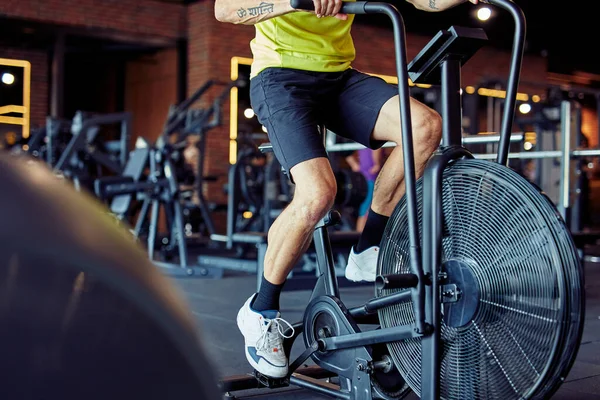 Cortado tiro de homem atlético em sportswear fazendo ciclismo em bicicletas de exercício no ginásio, treino cardio — Fotografia de Stock