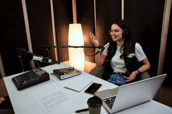 Portait de atractiva joven presentadora de radio que se ve alegre mientras habla en micrófono, moderando un espectáculo en vivo —  Fotos de Stock