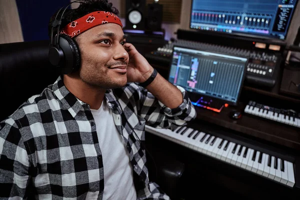 Joven, artista masculino con auriculares sonriendo mientras escucha música en un estudio de grabación — Foto de Stock