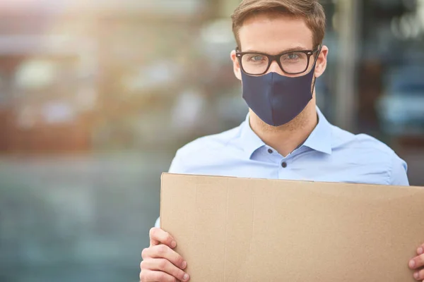 Retrato de un joven activista con máscara protectora negra sosteniendo un cartel vacío mientras estaba parado al aire libre durante el brote de coronavirus — Foto de Stock