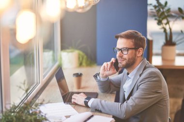 Önemli bir telefon. Laptop kullanan ve kafede uzaktan çalışan meşgul bir işadamının yan görüntüsü