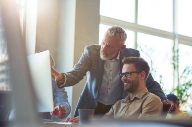 Modern ofiste masa başında oturmuş bilgisayar ekranına bakıyor ve projeyi tartışıyorlar. Kendinden emin, olgun bir adam genç iş arkadaşına bir şey anlatıyor.
