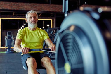 Kardiyo çalışması. Spor giyimli güçlü odaklı olgun bir sporcu spor salonunda kürek çekme makinesinde egzersiz yapıyor.