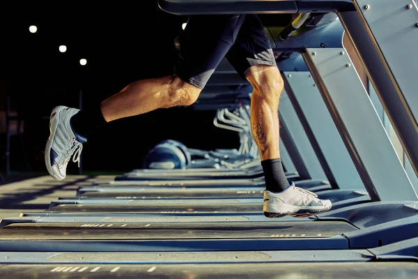 Faster and faster. Cropped shot of athletic man in sportswear running on a treadmill in a gym, focus on legs