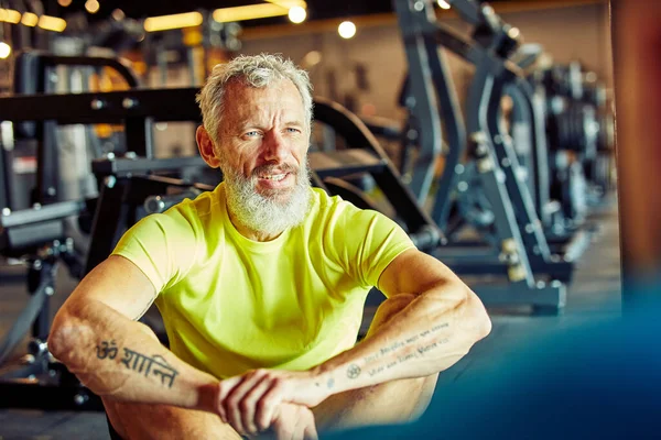 Retrato de um homem de meia-idade discutindo plano de treino com instrutor de fitness enquanto sentados juntos no chão no ginásio — Fotografia de Stock