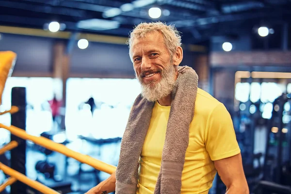 Descansar depois do treino de boxe. Retrato de um homem maduro bonito positivo em sportswear olhando para a câmera e sorrindo enquanto estava de pé no ringue no ginásio — Fotografia de Stock