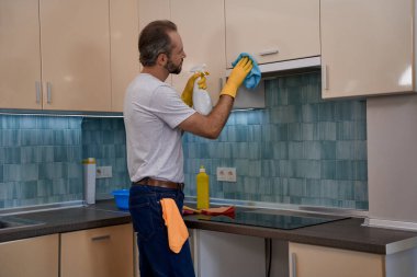 Delikanlı mobilyaların üzerinde deterjan ve bez kullanıyor.