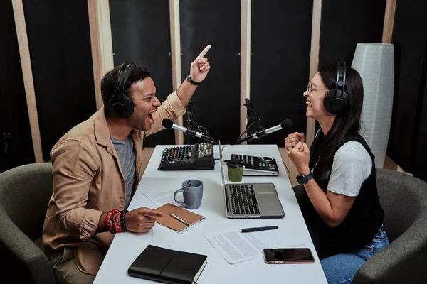 Portait de dos presentadores de radio, hombre y mujer jóvenes que se ven emocionales mientras hablan entre sí, moderando un espectáculo en vivo en el estudio —  Fotos de Stock