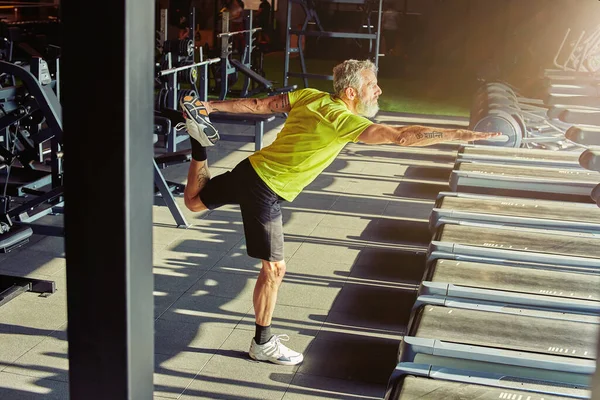 Exercícios de aquecimento. Tiro de comprimento total de um homem atlético maduro em sportswear fazendo exercícios de alongamento antes do treino em um ginásio — Fotografia de Stock