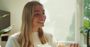 Neşeli bir kadın aydınlık ve canlı bitkilerle dolu bir odada lezzetli bir fincan çayın tadını çıkarıyor.