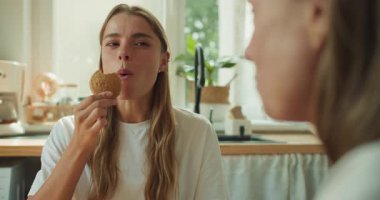 Güneşli bir mutfakta, iki neşeli kadın sıcacık bir anın tadını çıkarır. Kurabiyeler ve sıcak çay eşliğinde sohbet ederler.