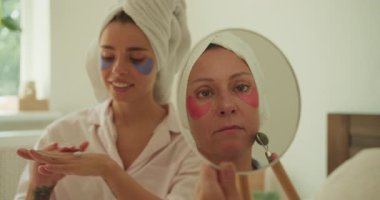 İki kadın renkli maskeler ve neşeli kahkahalarla dolu keyifli ve keyifli bir cilt bakımı yapıyorlar.