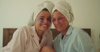 İki kadın, maske ve havlu takarak, gülücükler saçarak ve kahkahalarla spa gününün tadını çıkarırlar.