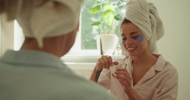 İki kadın, dingin bir banyoda canlı yüz maskeleri ve cilt ürünleriyle güzellik rutinlerinin keyfini çıkarıyorlar.