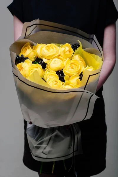 Çiçek buketi şeffaf bir paketin içinde çiçekçi bir kadının ellerinde. Rosa spreyi Catalina, rhamnus