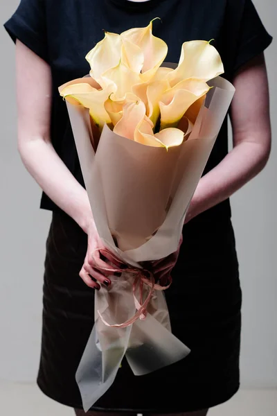 Çiçek buketi bej bir paketin içinde çiçekçi bir kadının ellerinde..