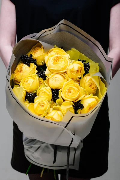 Çiçek buketi şeffaf bir paketin içinde çiçekçi bir kadının ellerinde. Rosa spreyi Catalina, rhamnus