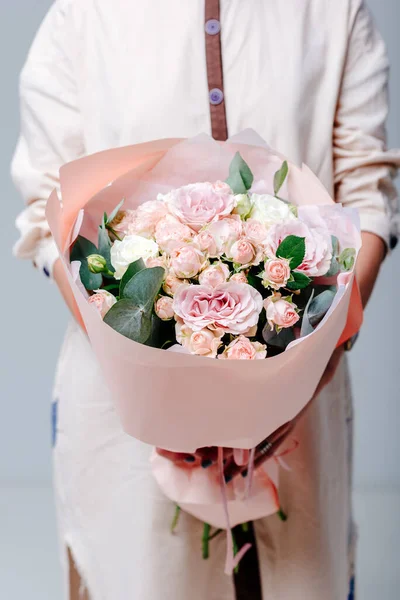 Çiçekçi bir kadının ellerinde pembe pakette bir buket çiçek. Gül, sprey gül, okaliptüs.