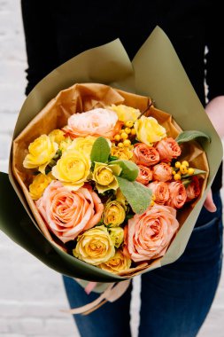 Fıstık rengi bir paketin içindeki çiçek buketi arka plandaki çiçekçi kadının elinde beyaz bir tuğla duvar. Rosa, merdivenler, ilex.