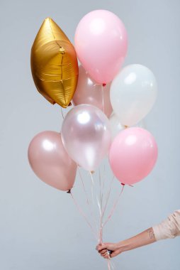 Beyaz, pembe, şeffaf helyum balonları ve altın yıldız karışımı beyaz arka planda bir kadının elinde..