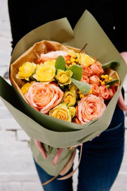 Fıstık rengi bir paketin içindeki çiçek buketi arka plandaki çiçekçi kadının elinde beyaz bir tuğla duvar. Rosa, merdivenler, ilex.
