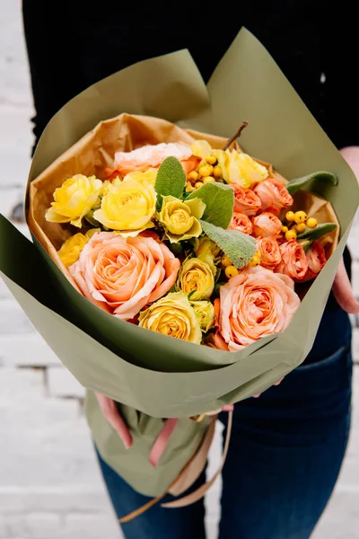 Fıstık rengi bir paketin içindeki çiçek buketi arka plandaki çiçekçi kadının elinde beyaz bir tuğla duvar. Rosa, merdivenler, ilex.