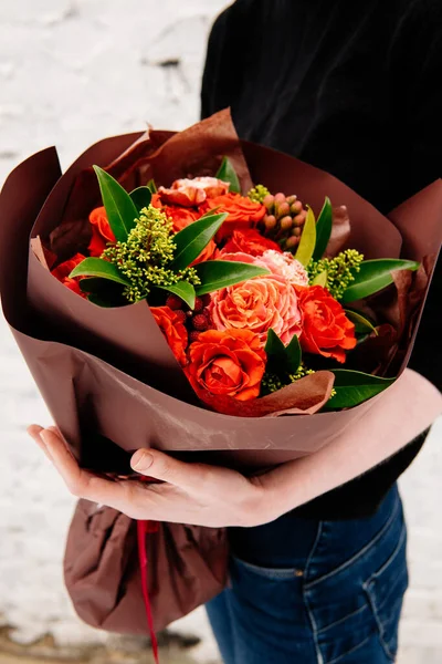 Burgundy paketindeki çiçek buketi arka plandaki çiçekçi kadının elinde beyaz tuğla bir duvar. Rosa, skimmy, karanfil, brunia.