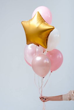 Beyaz, pembe, şeffaf helyum balonları ve altın yıldız karışımı beyaz arka planda bir kadının elinde..