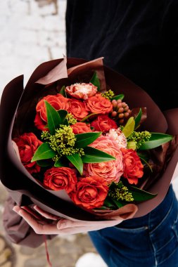 Burgundy paketindeki çiçek buketi arka plandaki çiçekçi kadının elinde beyaz tuğla bir duvar. Rosa, skimmy, karanfil, brunia.