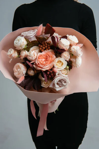 Bouquet of flowers in peach foamiran package in the hands of a woman florist on a light background. Rosa, cotinus, brunia, lagurus.