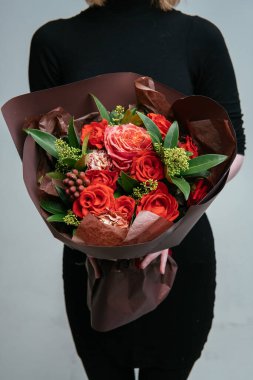 Çiçek buketi, açık arkaplanlı bir çiçekçinin elinde. Rosa, skimmy, karanfil, brunia.