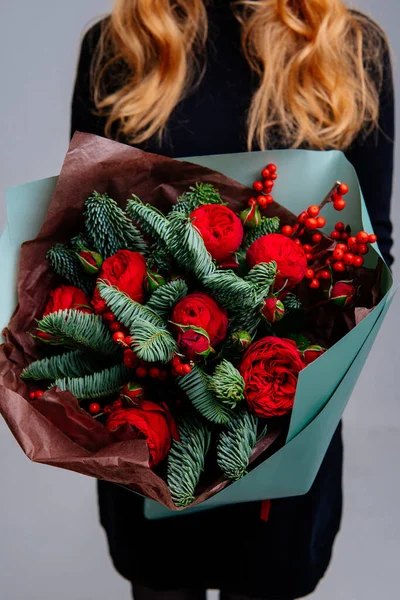 Zümrüt pakette bir buket çiçek, açık arkaplandaki kızıl saçlı çiçekçinin ellerinde. Gül, lex, ladin.