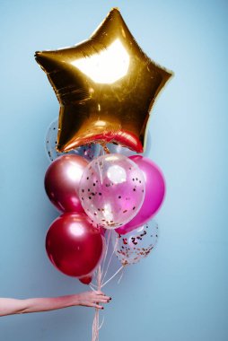 Beyaz, pembe, şeffaf helyum balonları ve altın yıldızın karışımı mavi arka plandaki bir kadının elinde..