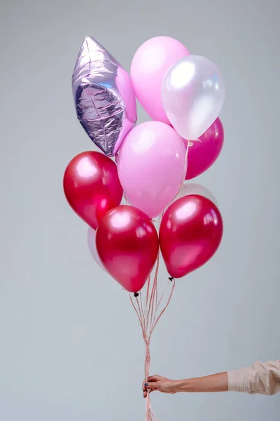 Kırmızı, pembe, şeffaf helyum balonları ve gümüş yıldızın bileşimi beyaz arka planda bir kadının elinde..