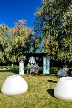 Gelin için fotoğraf çekilecek bir yer. Beyaz lüks sandalye, dışarıdaki yeşil çimenlikte bir ayna ve düğün çiçeği aranjmanının önünde duruyor.