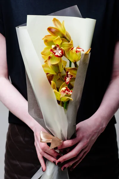 Çiçekçi bir kadının ellerinde bej pakette bir buket orkide..