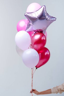 Kırmızı, pembe, şeffaf helyum balonları ve gümüş yıldızın bileşimi beyaz arka planda bir kadının elinde..