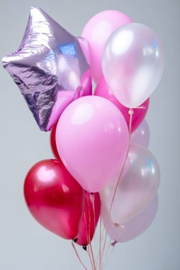 Beyaz zemin üzerinde kırmızı, pembe, şeffaf helyum balonları ve gümüş yıldız bileşimi.