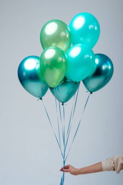 Açık yeşil, yeşil, zümrüt helyum balonları beyaz arka plandaki bir kadının elinde..