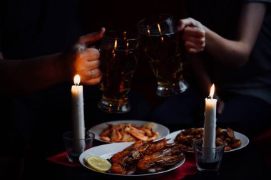 iki el, iki bardak bira, iki mum, karides ve limonlu ıstakoz kırmızı masa örtüsü.