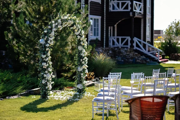 Açık havada düğün hazırlığı, pastel beyazı çiçeklerle süslenmiş düğün kemeri beyaz sandalyeli Kyavari.