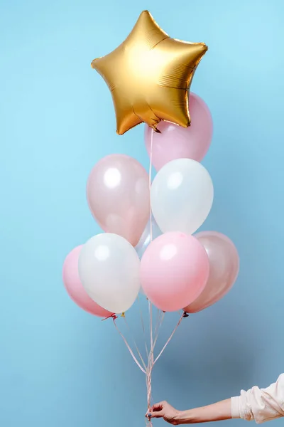 Beyaz, pembe, şeffaf helyum balonları ve altın yıldızın karışımı mavi arka plandaki bir kadının elinde..