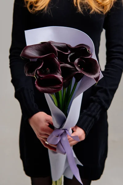 Bouquet of calla lilies in lilac foamiran package in the hands of red-haired girl florist on light background.