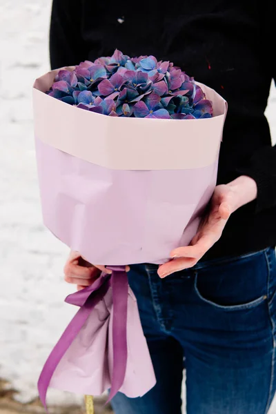 Mor pakette bir buket ortanca çiçekçi kadının ellerinde beyaz tuğladan bir duvar..