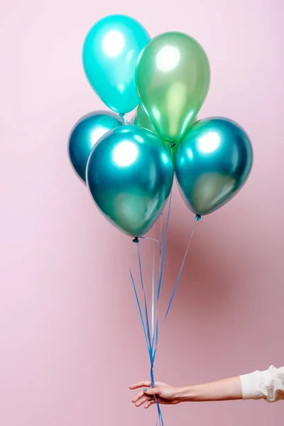 Açık yeşil, yeşil, zümrüt helyum balonları pembe arka plandaki bir kadının elinde..