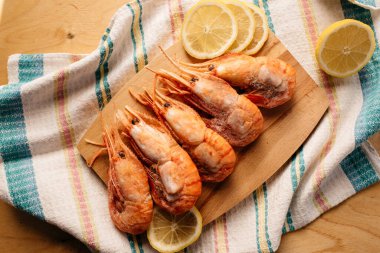 Çizgili bir masa örtüsünün üzerinde tahta bir tahtada botan karidesi ve limon.